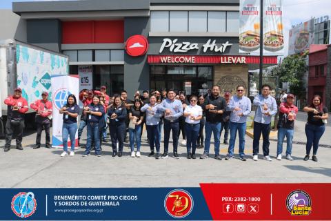 Varias personas sonriendo para una foto con un Pizza Hut al fondo. 