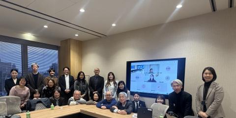 Several people smiling for a photo with online participants on a screen behind them. 